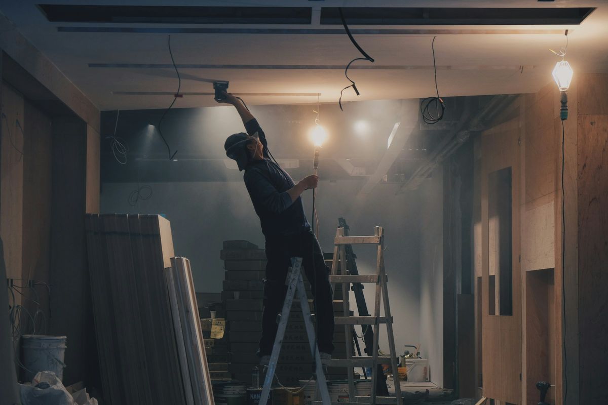 Een elektricien op een ladder hangt lampen op tijdens een verbouwing