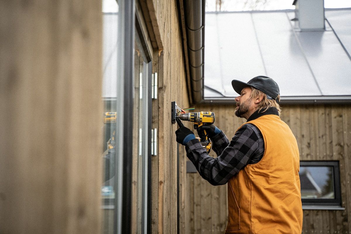 Een vakman schroeft een buitenlamp vast aan een houten gevel